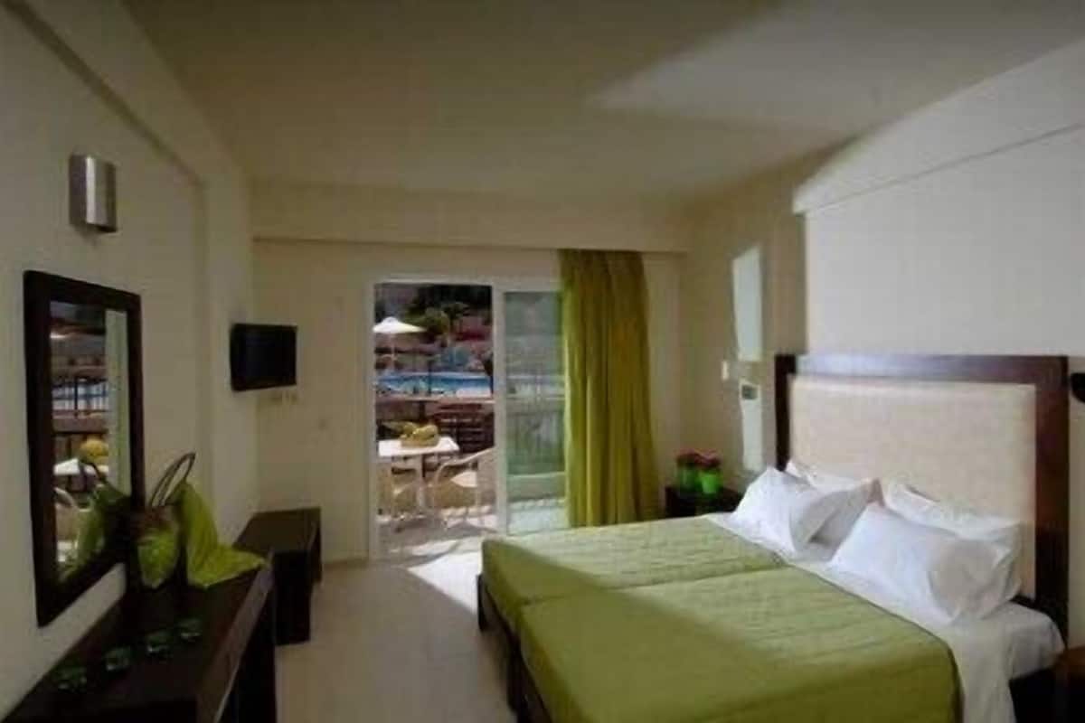 Habitación de hotel con cama, escritorio, silla, televisor y vista a un área exterior con piscina.