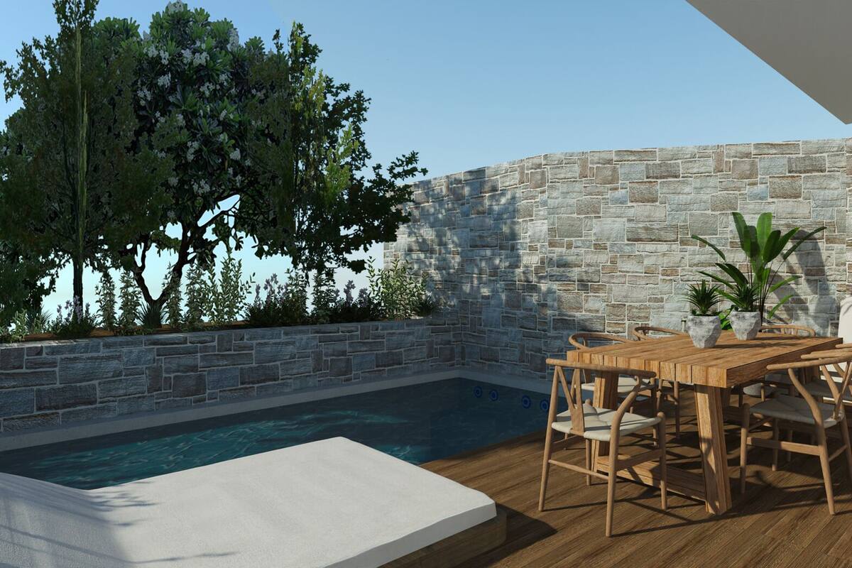 Zona junto a la piscina con pared de piedra, mesa de madera con sillas y un banco blanco.