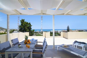 A terrace with a table set for dining, a lounge area, and a view of the sea. - Rainbow Apartments (Hersonissos)