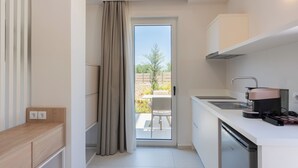 A modern kitchen with a built-in dishwasher, a coffee machine, and a sliding glass door leading to an outdoor patio. - Rainbow Apartments (Hersonissos)