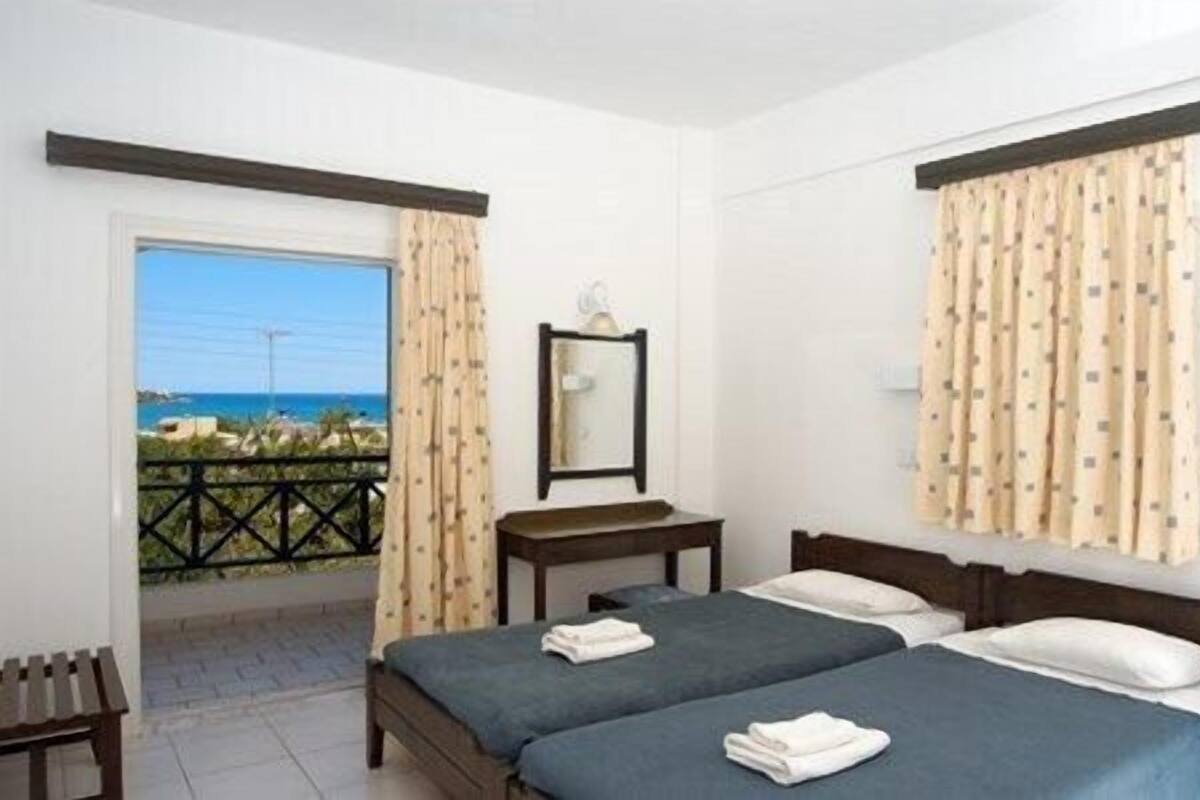 Habitación de hotel con dos camas, una mesita, un espejo y vista al mar.