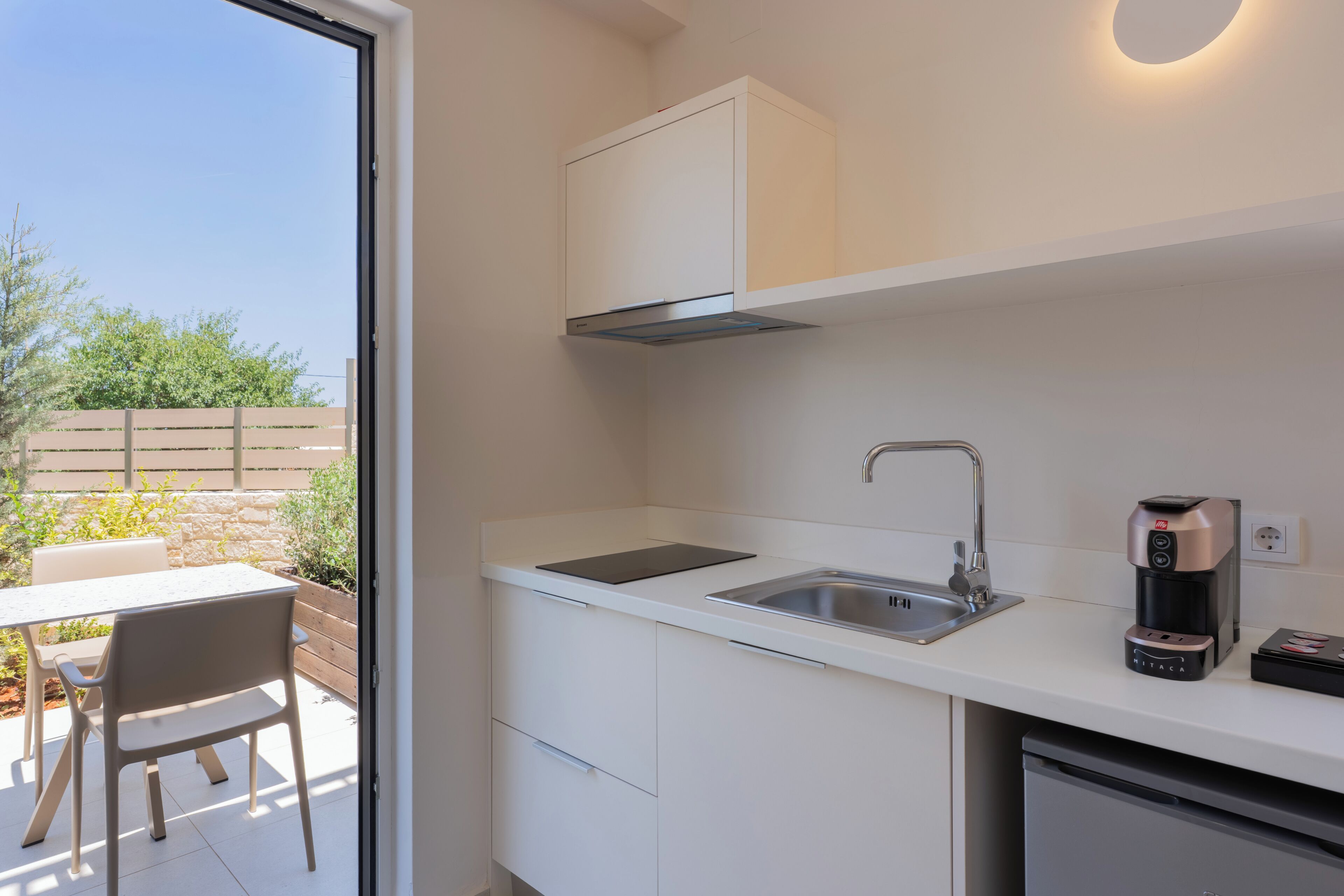 A compact kitchen with a built-in dishwasher, a coffee maker, and a window overlooking a garden.