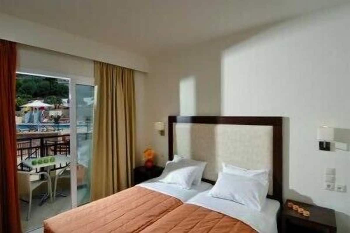Habitación de hotel con cama, mesita de noche y vista a un espacio exterior con mesas y sillas.