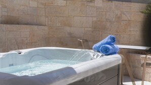 A hot tub with water, a towel, and a stone wall in the background. - Rainbow Apartments (Hersonissos)