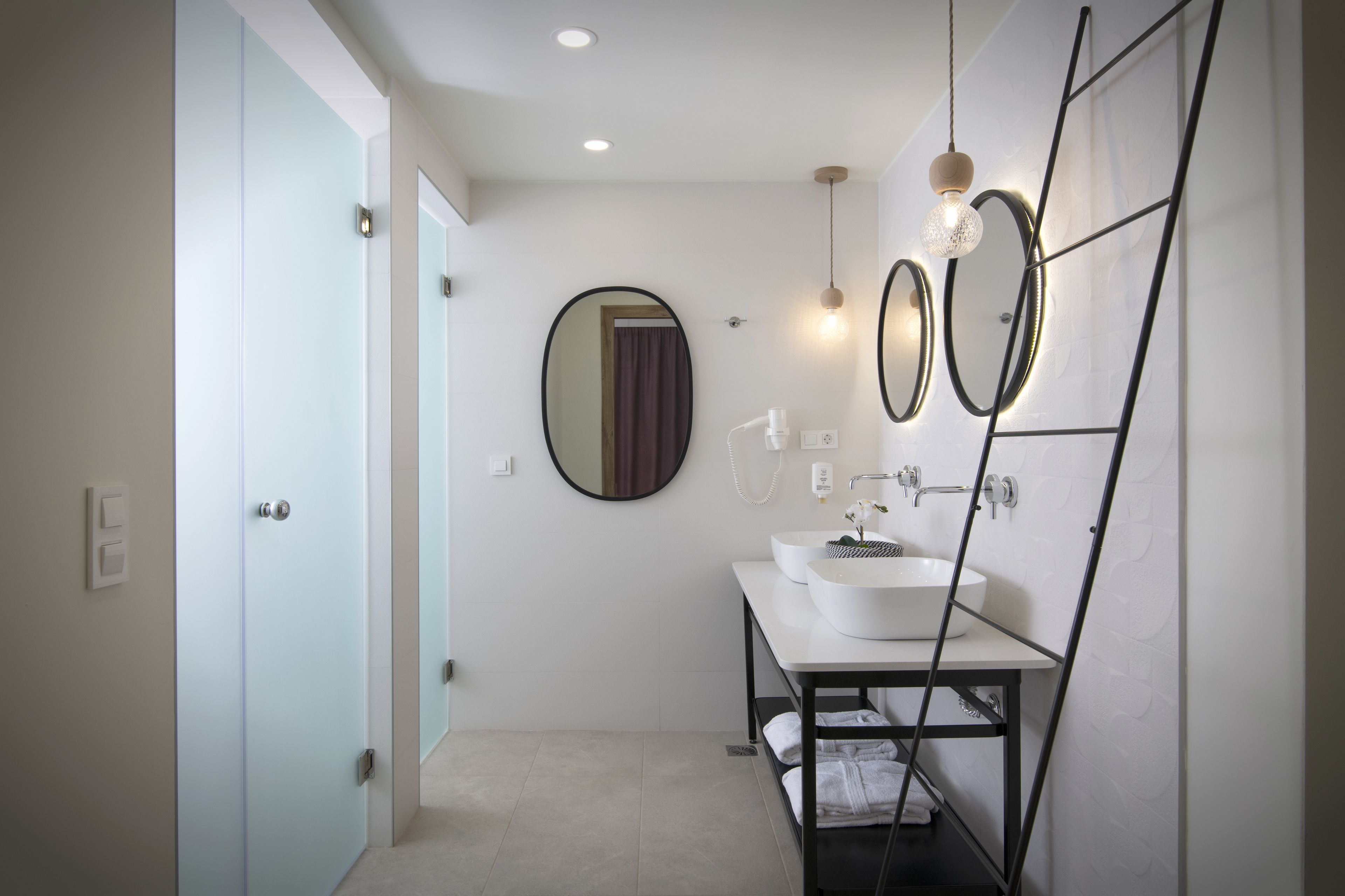 A modern bathroom with a light blue door, a round mirror, two sinks, and a towel rack.