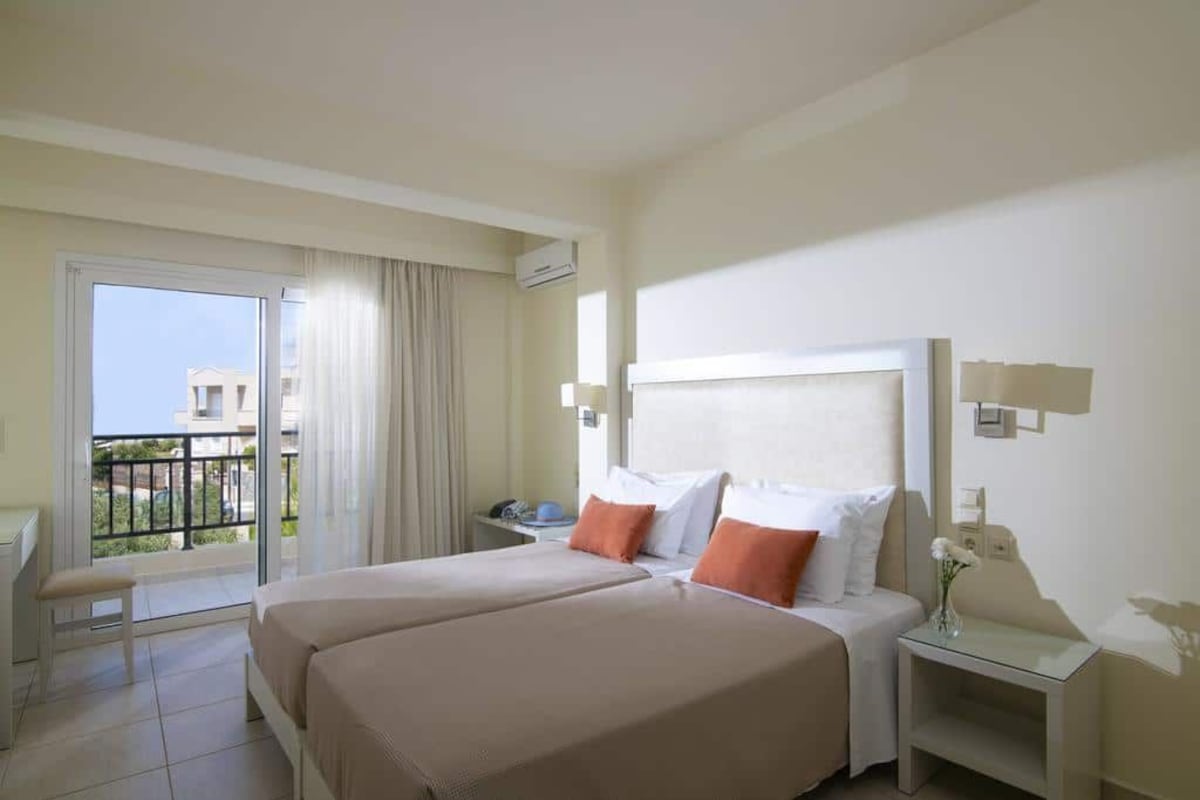 A hotel room with a large bed, a bedside table, a nightstand, a chair, and a balcony with a view of buildings.