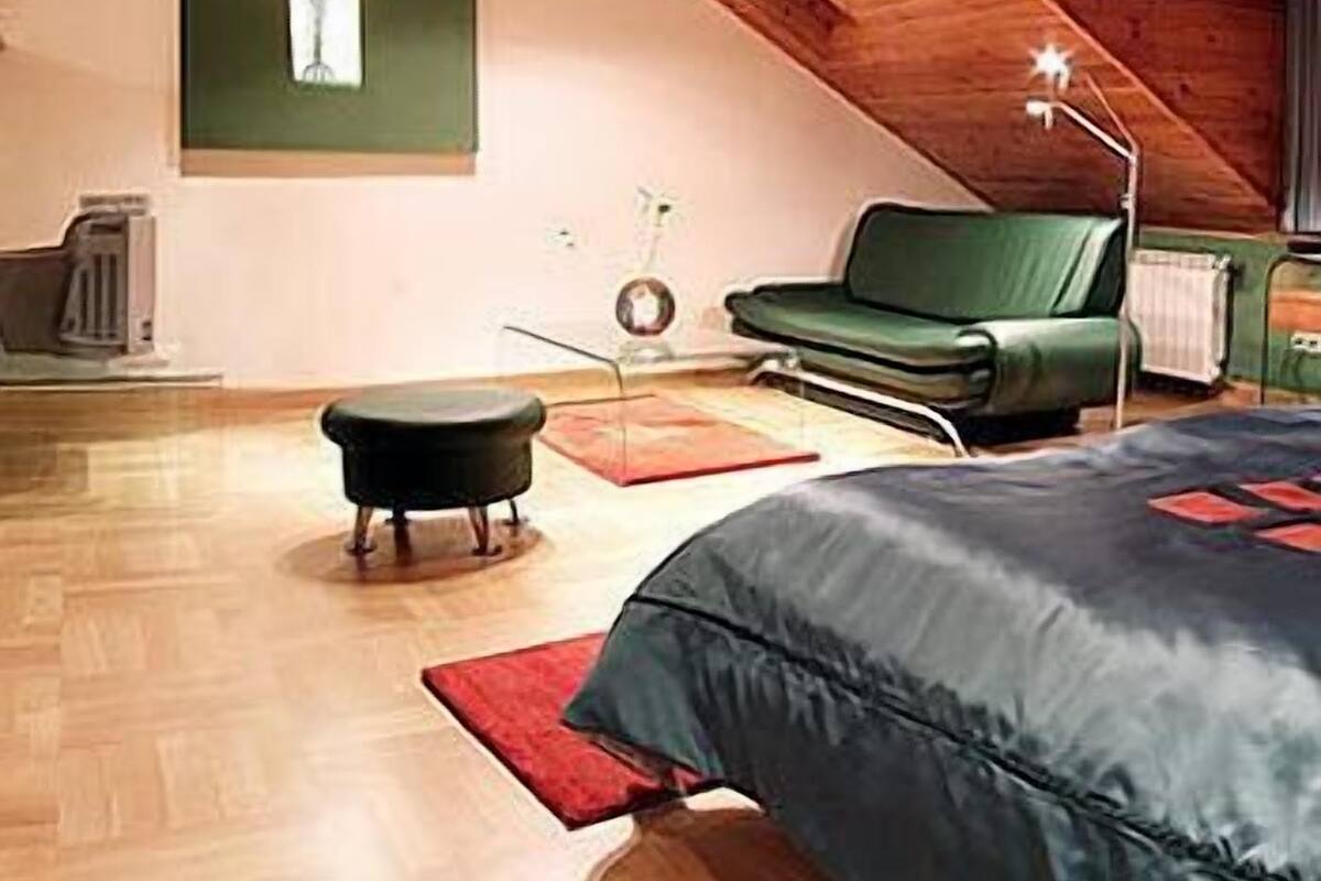 A room with a sloped ceiling, a green sofa, a small table, a lamp, and a radiator.