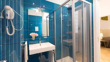 A bathroom with a blue tiled wall, a white sink, a mirror, and a glass-enclosed shower.
