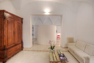 Una sala de estar con un aparador de madera, un sofá color beige, una mesa de centro con libros y una orquídea en maceta.