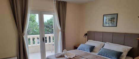 Una habitación de hotel con una cama, una mesita de noche de madera, una pequeña mesa y un balcón con barandilla.