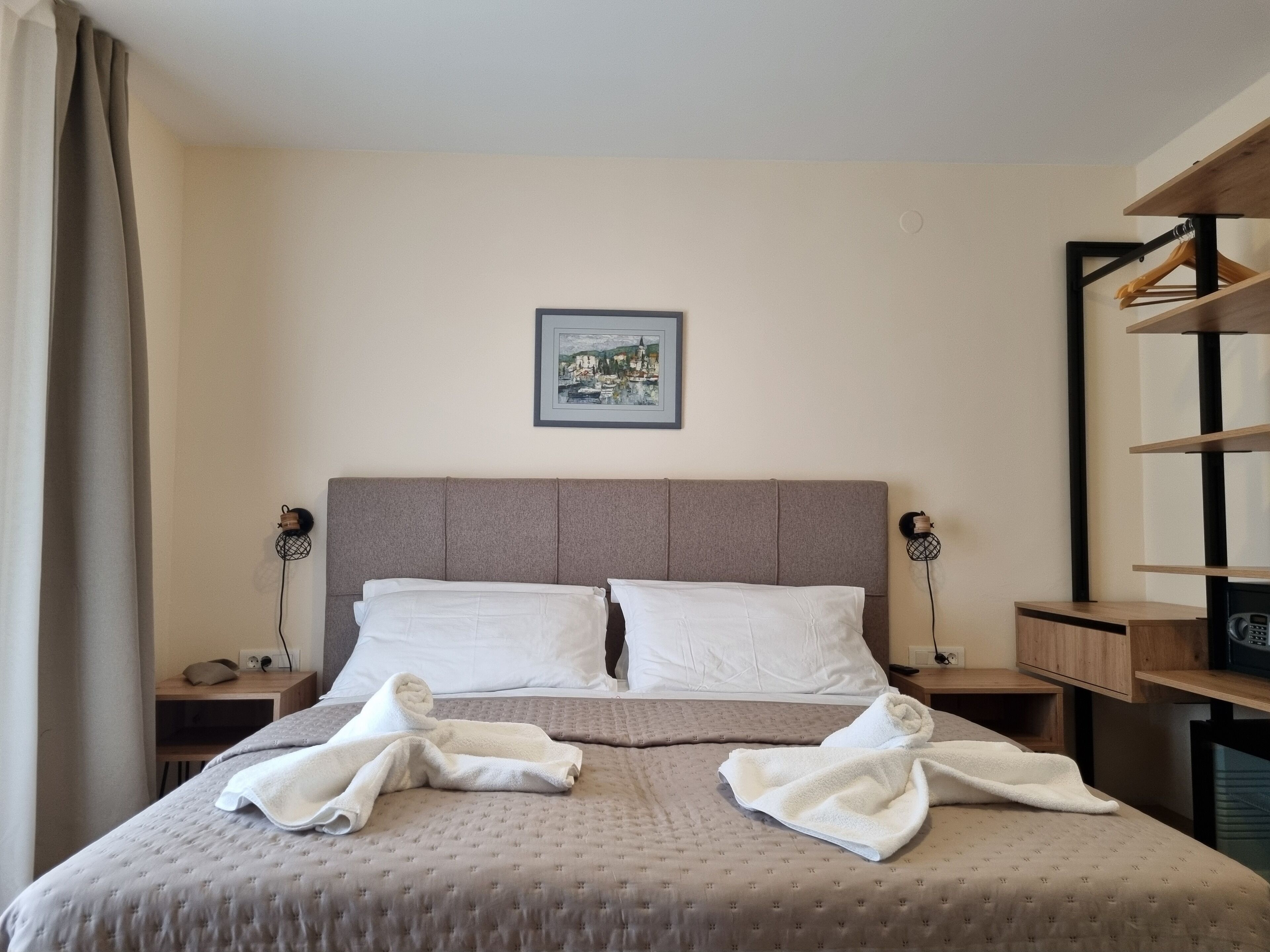 A hotel room with a large bed, two bedside tables, a headboard, a framed picture on the wall, and a wooden shelf unit.
