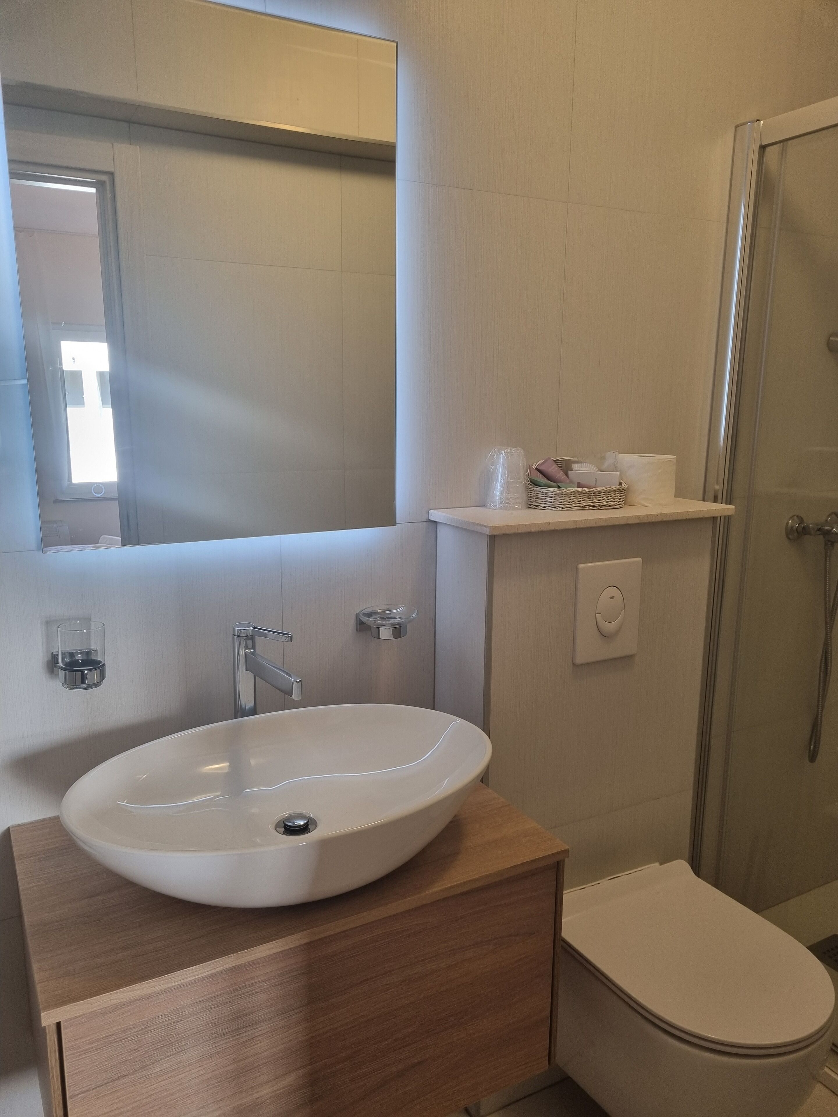 Ein Badezimmer mit einem weißen Waschbecken, einem Holzkosmetikschrank, einem Spiegel, einer Toilette und einer Duschkabine aus Glas.