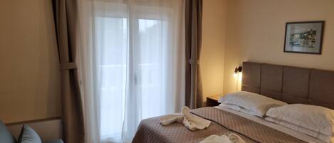 Een hotelkamer met een bed, nachtkastje, lamp, schilderij aan de muur en een raam met gordijnen.