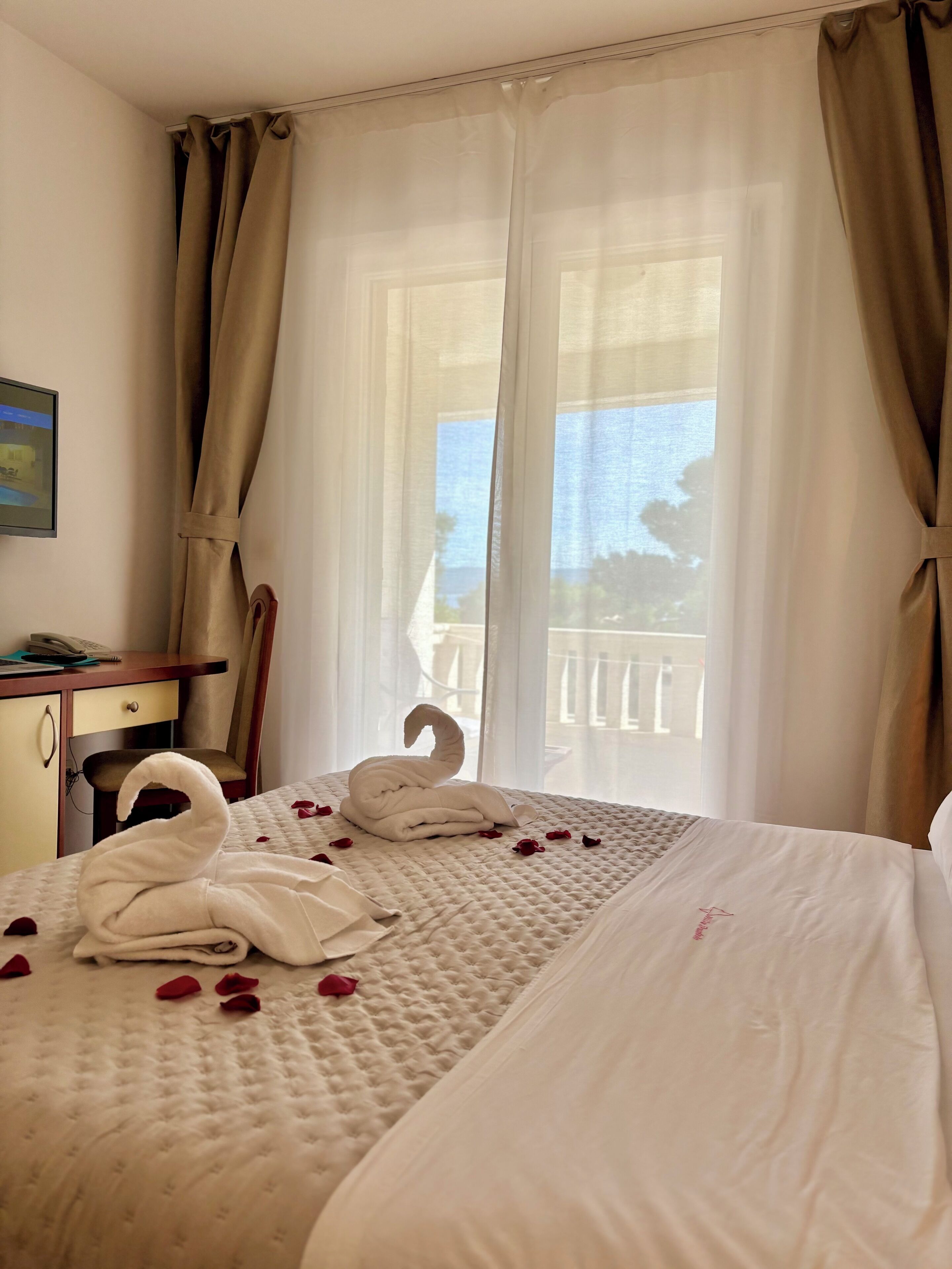 A hotel room with a bed, a desk, and a view of the sea.