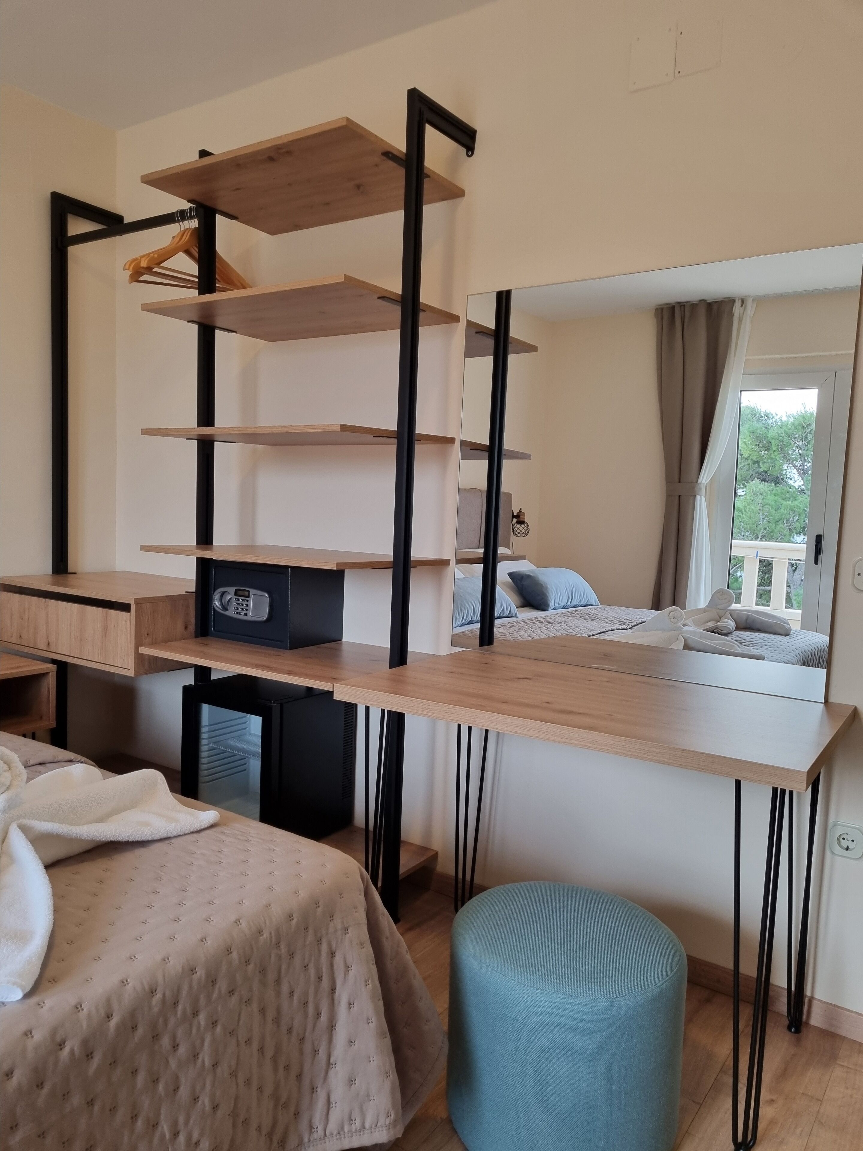 A bedroom with a wooden desk, shelves, a mirror, and a bed with a blue pillow.