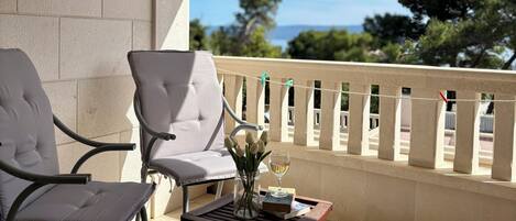 A balcony with two chairs, a small table, and a view of the sea.