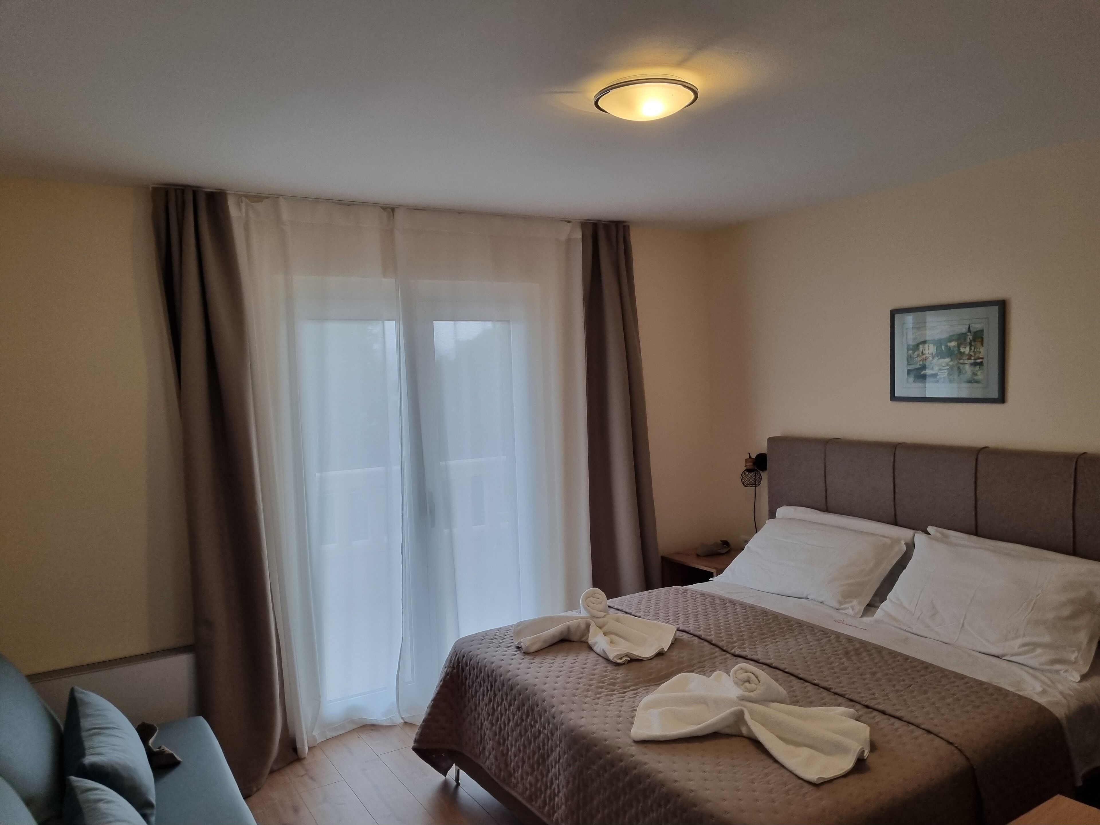 Une chambre d’hôtel avec un lit, une table de chevet, une lampe, un tableau au mur et une fenêtre avec des rideaux.