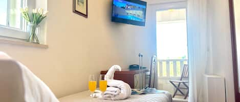 A hotel room with a bed, a TV mounted on the wall, a window with a view, and a balcony with a chair.