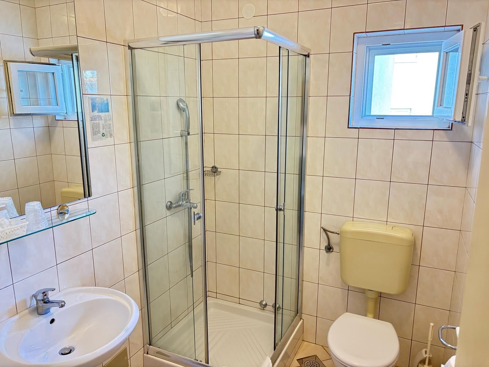 A bathroom with a glass-enclosed shower, a sink, a toilet, and a window.