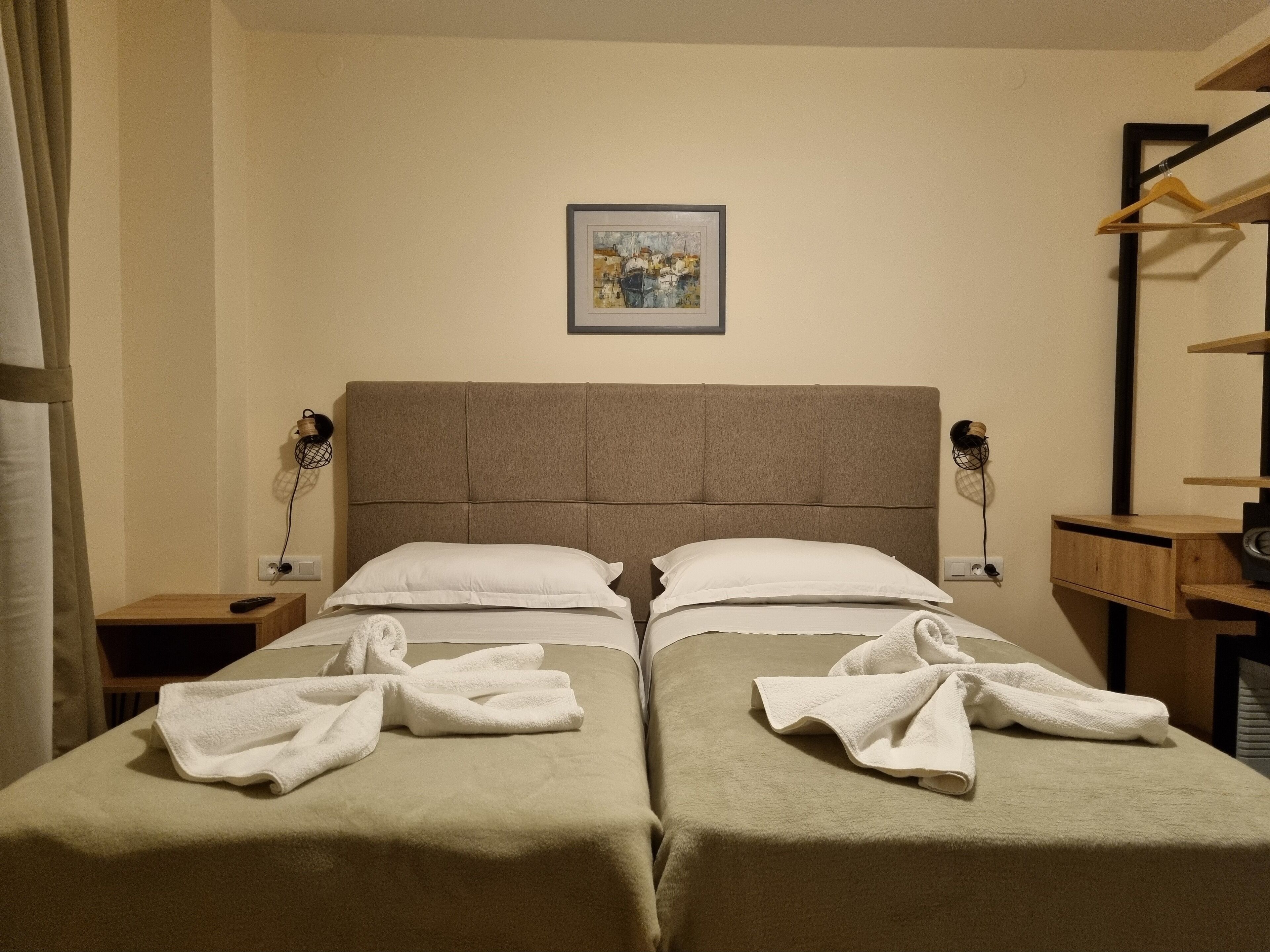 A hotel room with two beds, a painting on the wall, and a wooden shelf unit.