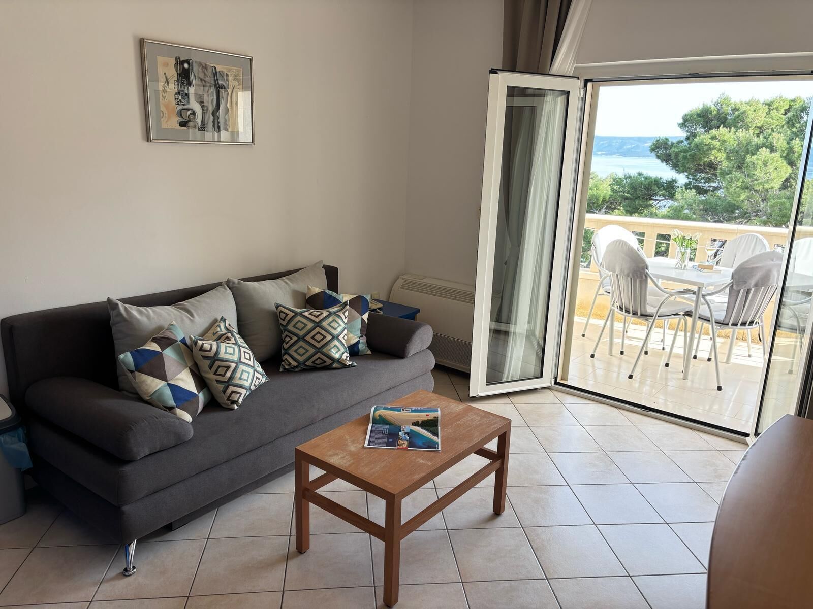 A living room with a sofa, cushions, a coffee table, and a sliding glass door leading to an outdoor patio with chairs and a table.