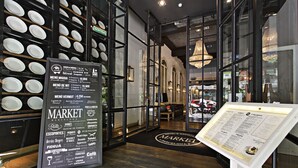 Interior de restaurant amb un tauler de menús negre que mostra diversos plats i preus, una entrada amb porta de vidre i un penjador.