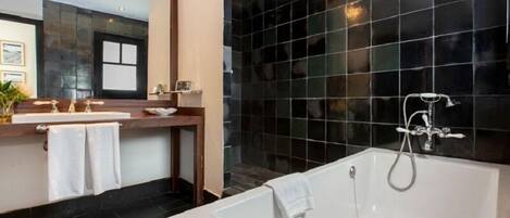 A modern bathroom with a large bathtub, two sinks, and a dark tiled wall.