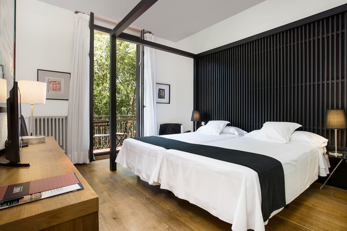 Habitación de hotel con una cama grande, un escritorio con lámpara y vistas a zonas verdes.