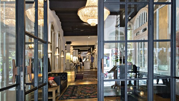 Rebedor d'hotel amb entrada de vidre, un lluminària central i un sòl amb moqueta.