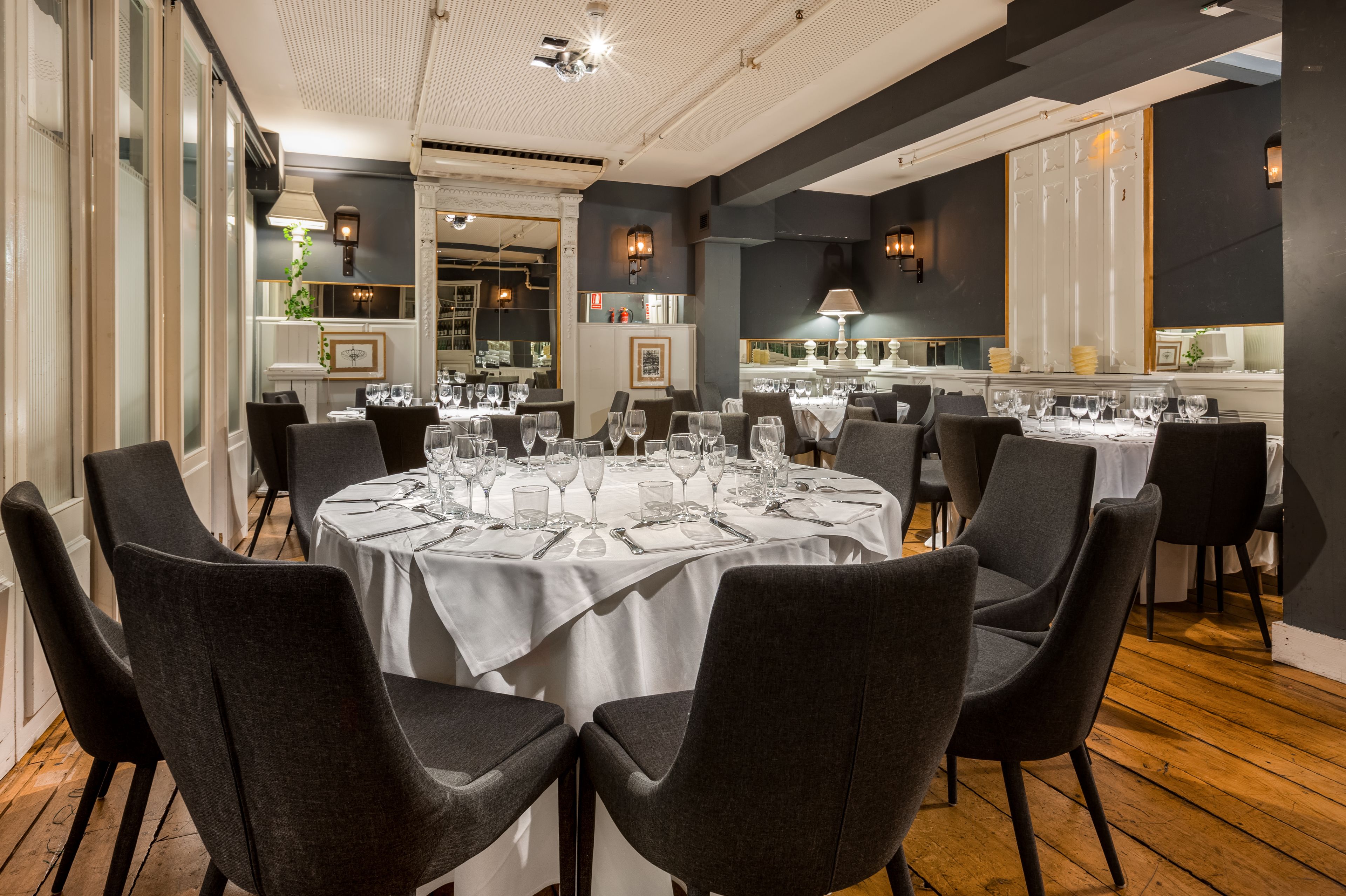 A restaurant with round tables set for dining, featuring a modern interior design with dark walls and wooden flooring.