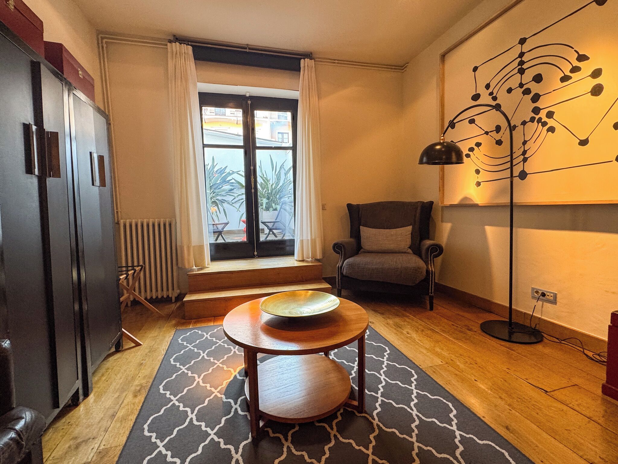 Un espacio habitable compacto con kitchenette, una zona de comedor con una mesa pequeña, una silla y una lámpara de pie.