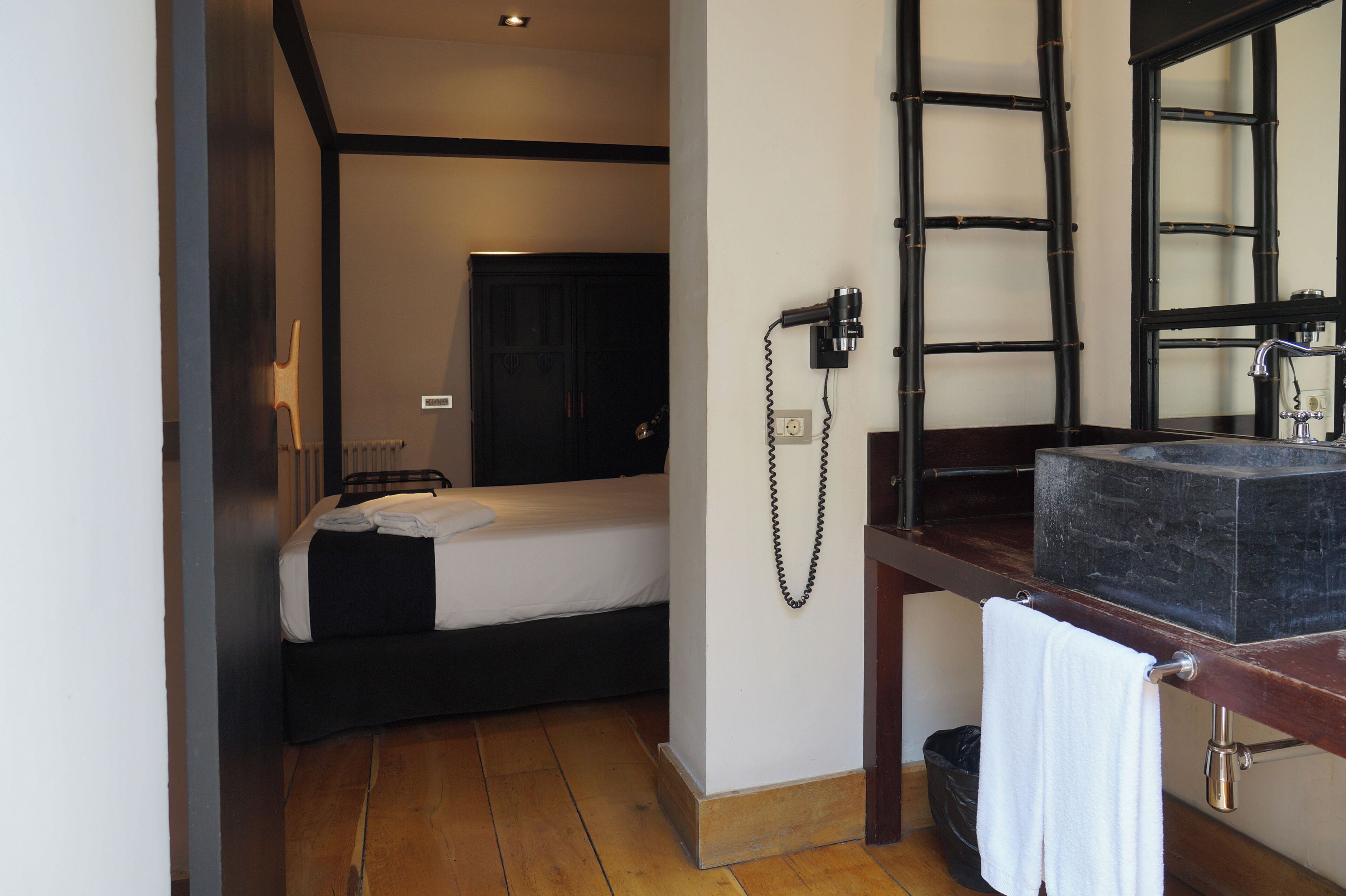 Ein Hotelzimmer mit einem Bett, einem Nachttisch mit Lampe, einem Spiegel und einem Badezimmer mit Waschbecken und Handtuchhalter.