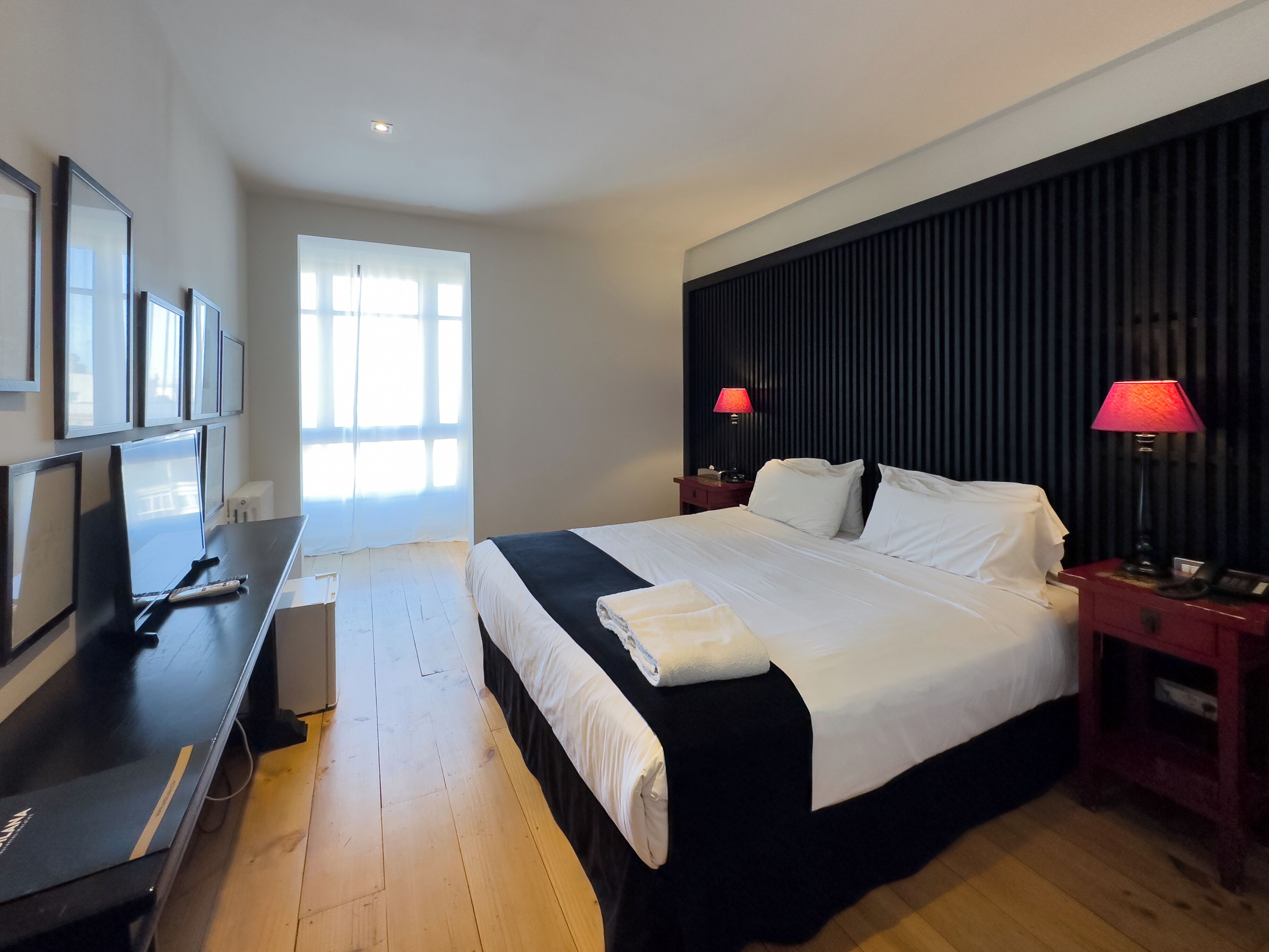 A modern hotel room with a large bed, a flat-screen TV, and a desk with a computer.