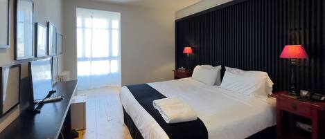 A modern hotel room with a large bed, a flat-screen TV, and a desk with a computer.