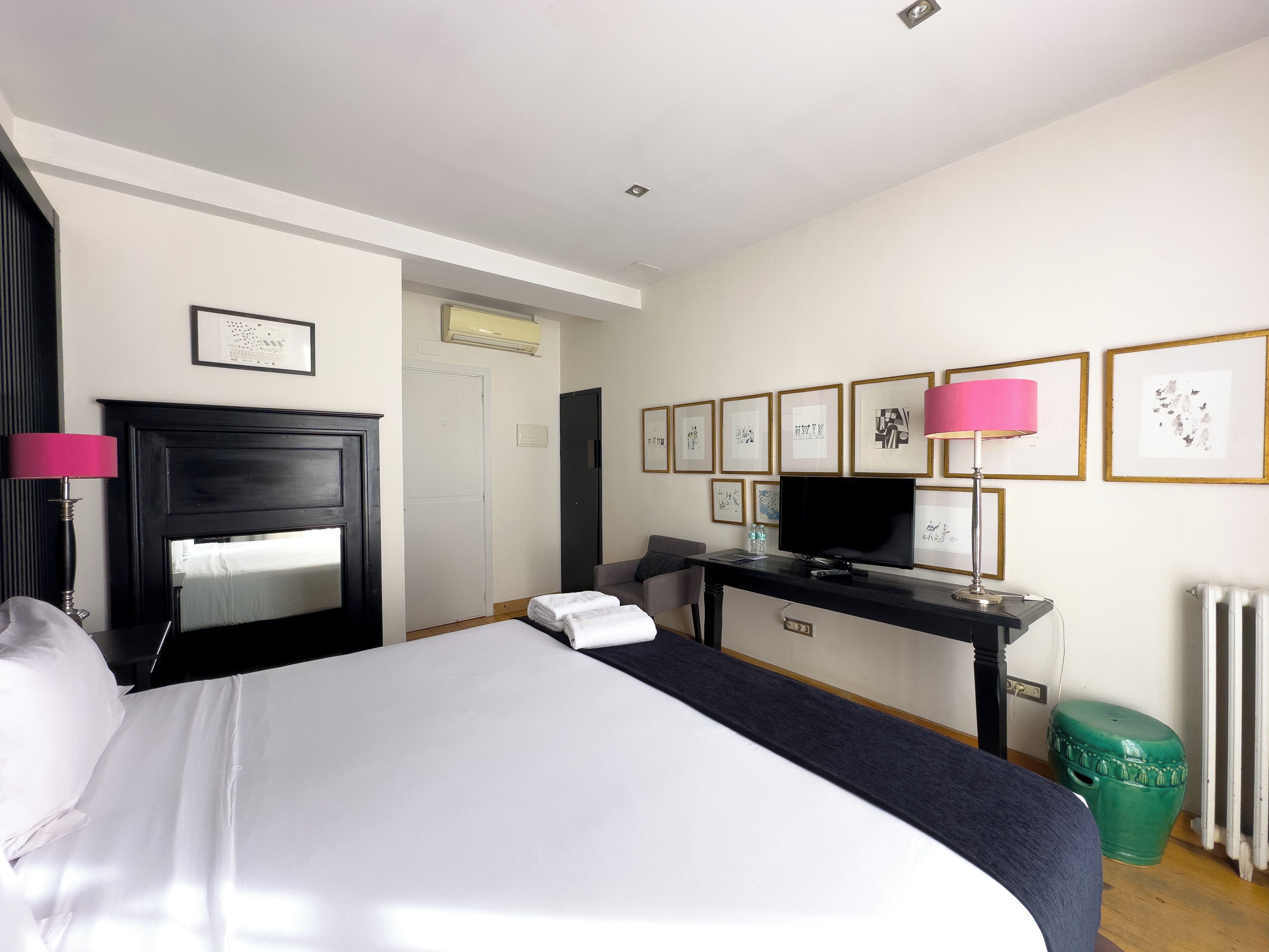 Une chambre d’hôtel avec un lit, un bureau avec une télévision, une chaise, un radiateur et des tableaux encadrés au mur.
