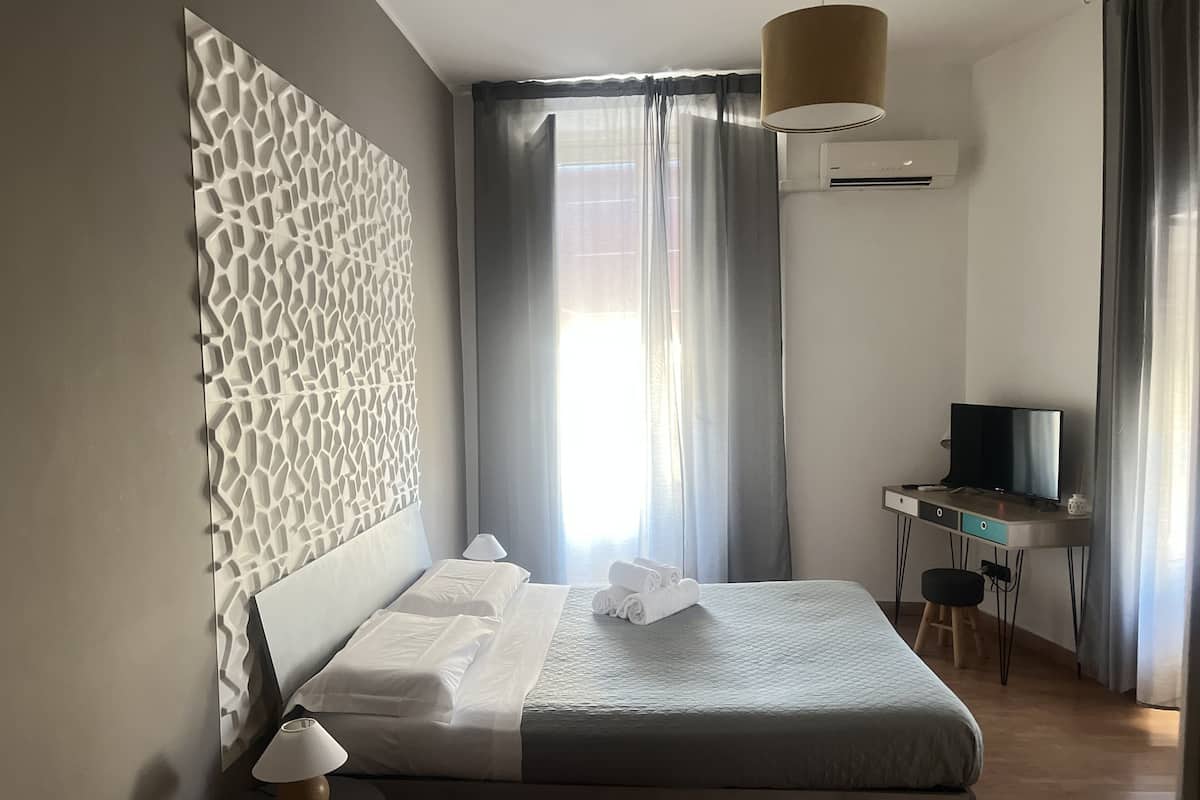 Ein modernes Schlafzimmer mit Bett, Schreibtisch, Fernseher und einem Fenster mit Vorhängen.