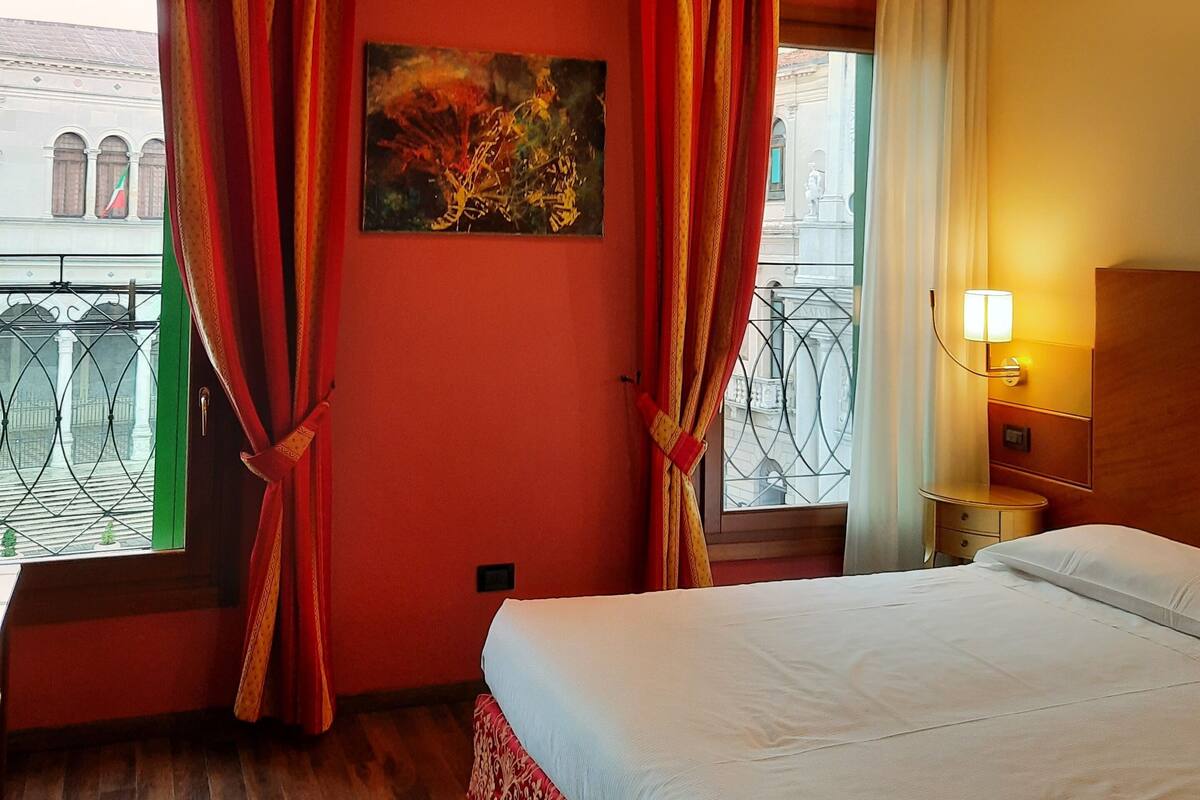 Ein Hotelzimmer mit Bett, einem Bild an der Wand und einem Fenster mit Vorhängen.