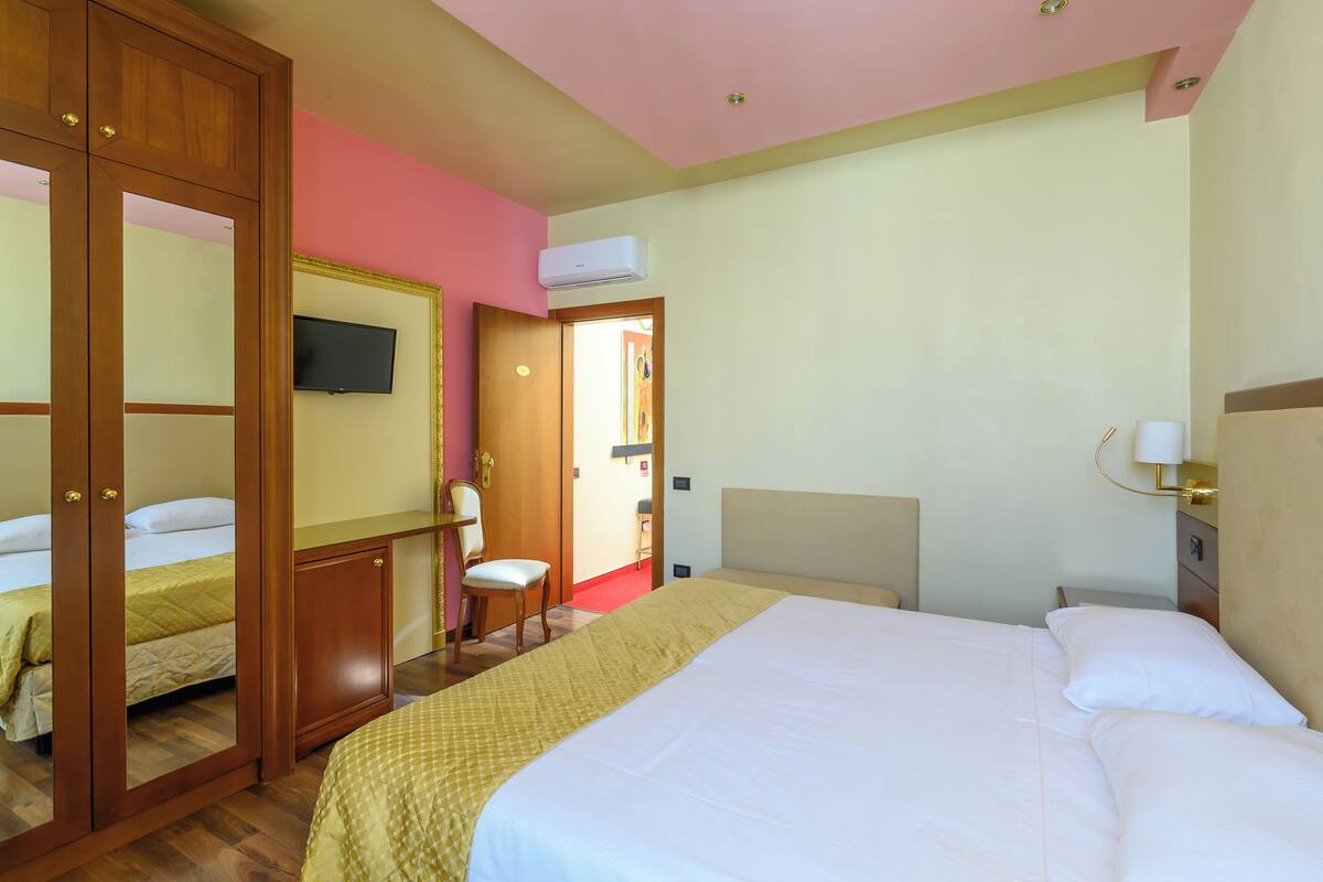Ein Hotelzimmer mit Bett, Sessel, Kleiderschrank, Fernseher und Klimaanlage.