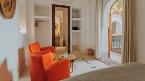 A modern room with orange chairs, a small table, and a view of an outdoor area with a palm tree. - Riad Djebel (Marrakech)