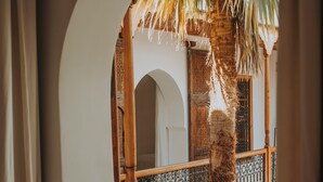 An arched doorway leading to a balcony with a palm tree, a wooden railing, and a patterned metal fence. - Riad Djebel (Marrakech)