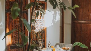 A dining area with a table set for two, surrounded by wooden doors and a hanging light fixture. - Riad Djebel (Marrakech)