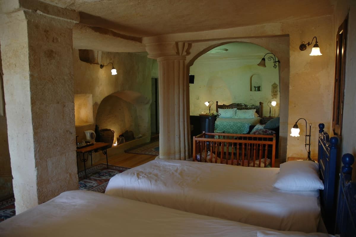 A bedroom with two beds, a wooden crib, a small table, and a mirror.