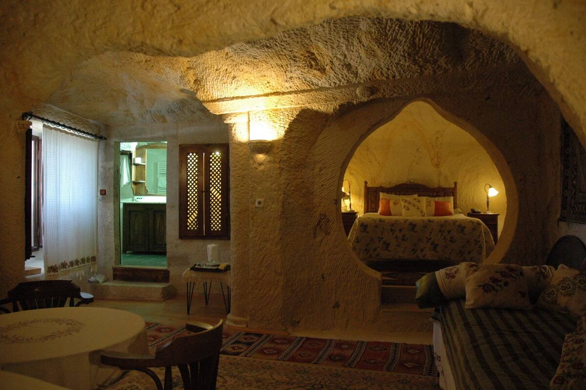A cozy room with a stone archway, a bed with floral bedding, a small table, and a chair.