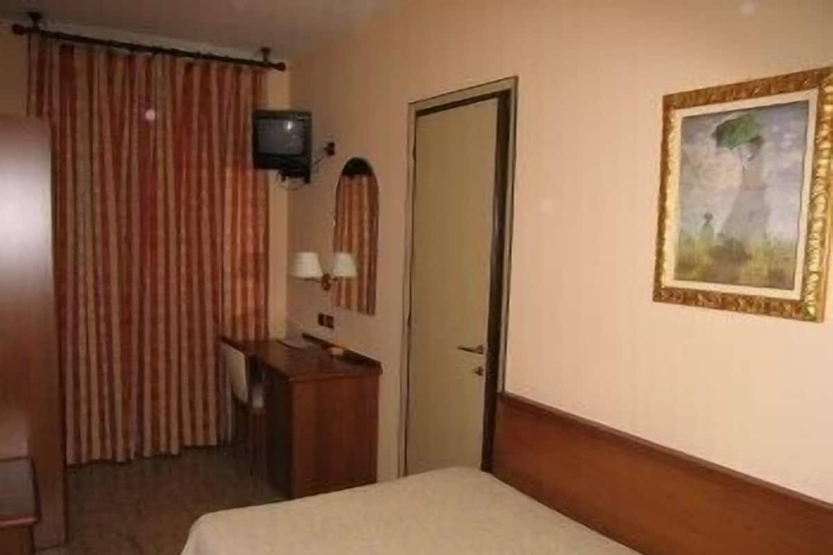 Ein Hotelzimmer mit Bett, Schreibtisch mit Stuhl, Fernseher, einer Tür und einem Bild an der Wand.