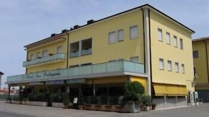 Un immeuble jaune avec un balcon au deuxième étage, une enseigne indiquant « Hôtel Le P’tit P’tit », et des plantes en pot devant l’entrée.
