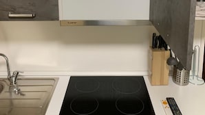 Une cuisine équipée d’une cuisinière intégrée, d’un évier et d’une étagère contenant des ustensiles de cuisine.