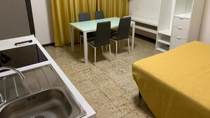Une petite chambre d’hôtel avec une kitchenette, une table à manger avec des chaises, un lit recouvert d’une courtepointe jaune, un téléviseur fixé au mur et une armoire.