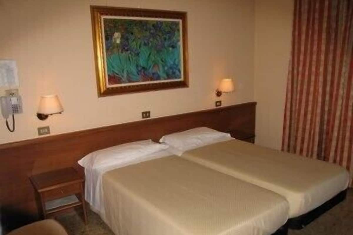 Ein Hotelzimmer mit zwei Betten, einem Nachttisch, einer Lampe, einem Wandbild und einem Telefon.