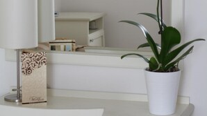 Un baño con tocador blanco, un espejo, una orquídea en maceta y un cuadro en la pared.