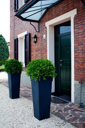 Un bâtiment en briques avec une porte verte, un auvent noir et deux grands jardinières contenant des arbustes verts.